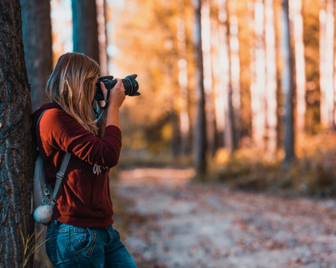woman leaning back on tree trunk using black dslr camera during day