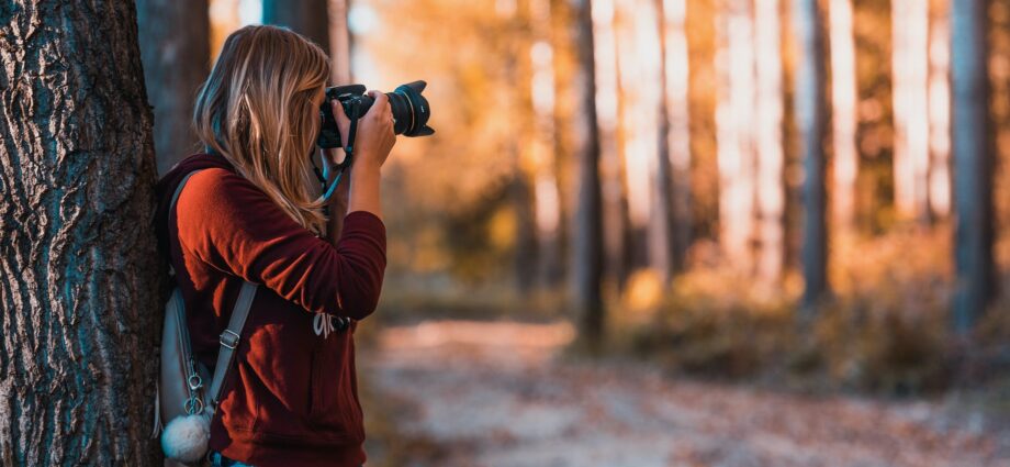woman leaning back on tree trunk using black dslr camera during day