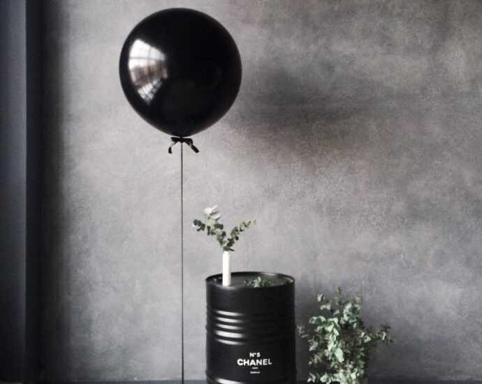 grayscale photography of balloon beside chanel metal barrel