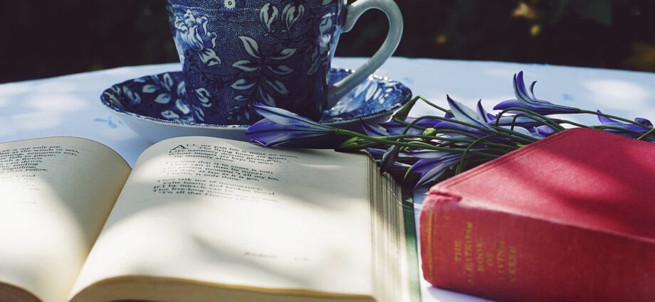 book opened on top of white table beside closed red book and round blue foliage ceramic cup on top of saucer