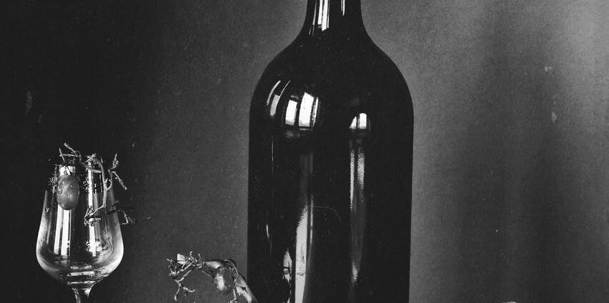 black wine bottle and wine glass beside fruits