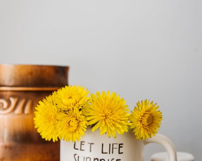 yellow dandelions placed in light mug against wall