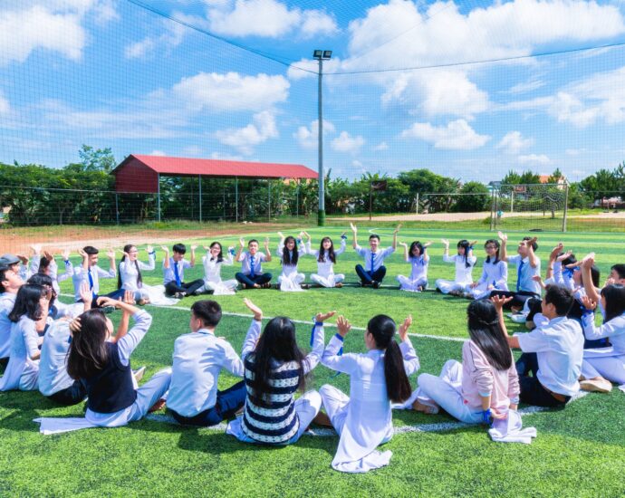 people sitting on green lawn grass while doing hands up at daytime