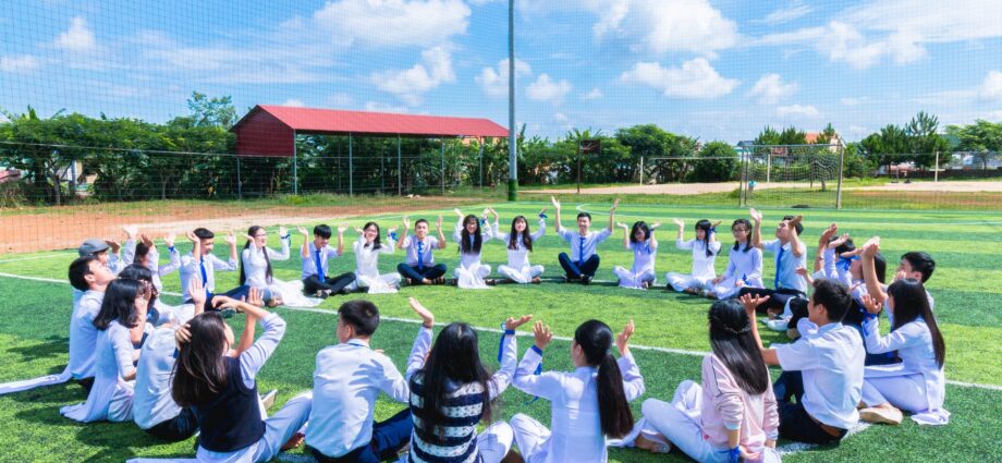people sitting on green lawn grass while doing hands up at daytime